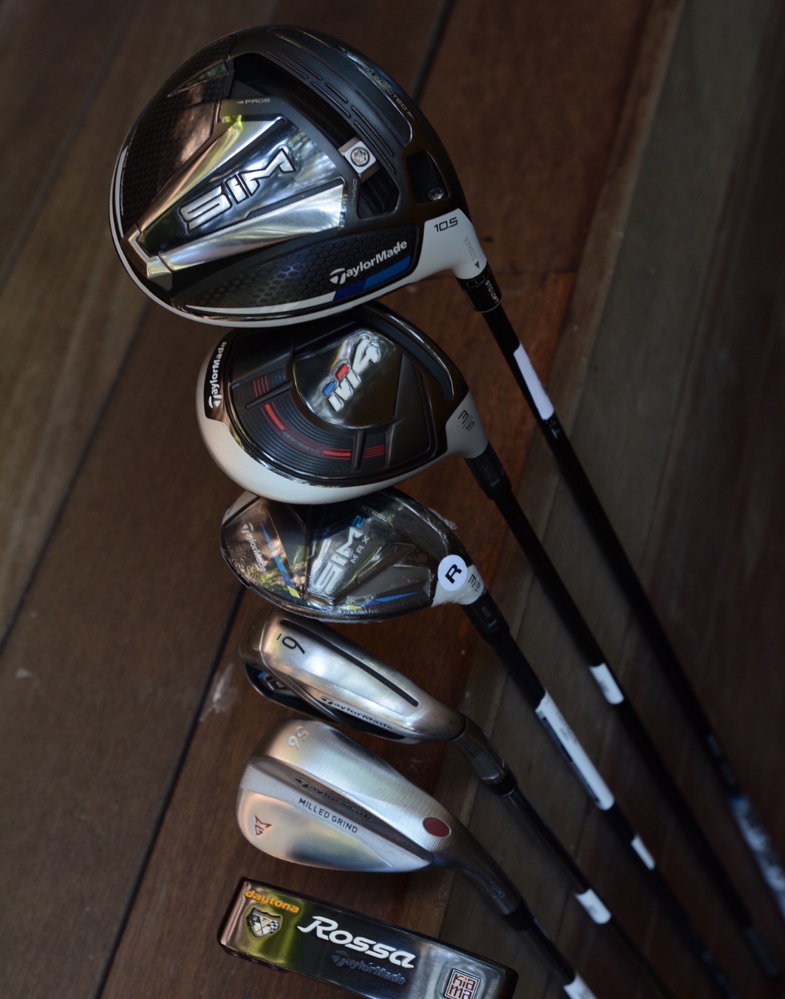 6 different golf clubs lined up vertically along a brown background. taylormade full set