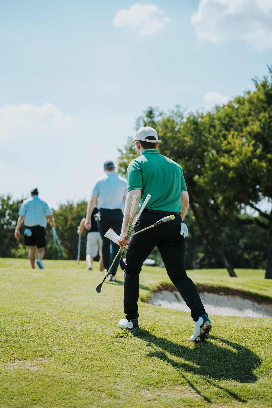 Foursome walking the fairway toward a green, one player carrying clubs